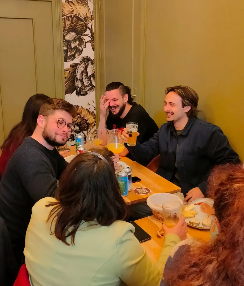 Groupe de personnes trinquant leurs bières artisanales assis autour de tables en bois