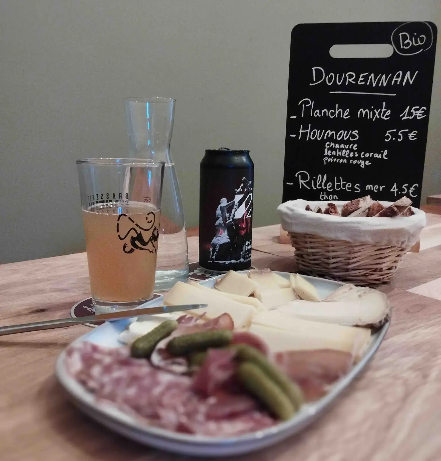 Planche de charcuterie et de fromage devant une cannette de bière artisanale et un menu sur ardoise
